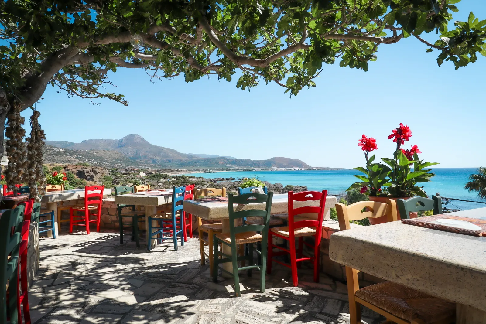 A taverna terrace with painted wooden chairs looking out over Falasarna beach in western Crete