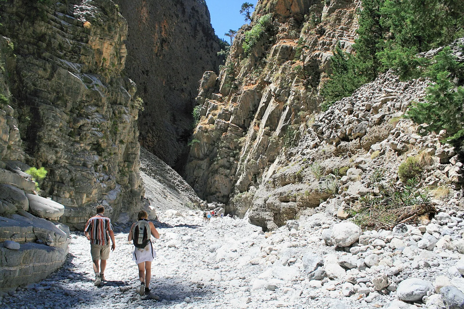 Hikers walking between towering rock walls in the Samaria Gorge on the island of Crete, Greece