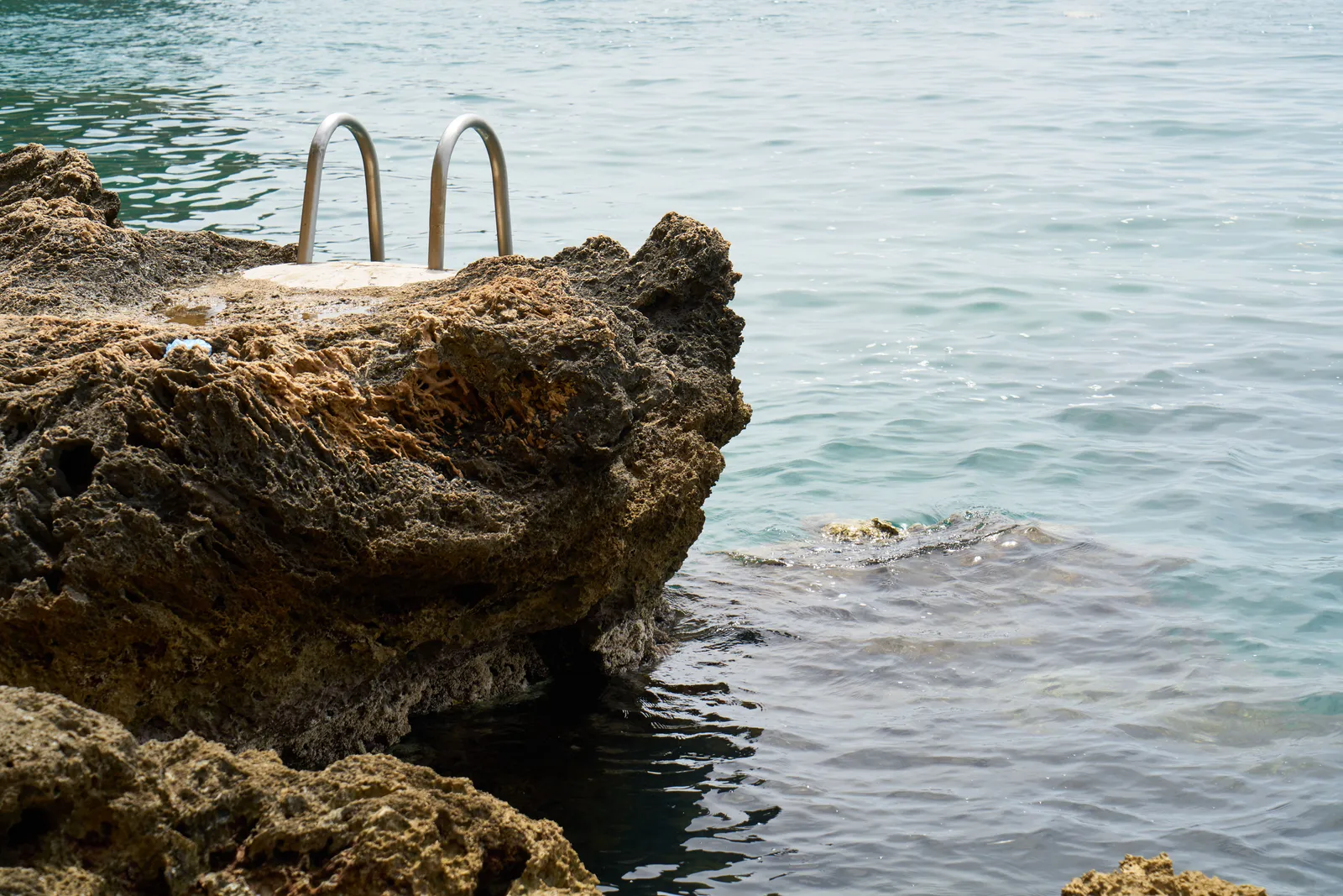Rocky swimming platform with a ladder into clear water along Hydra's coastal path, Greece