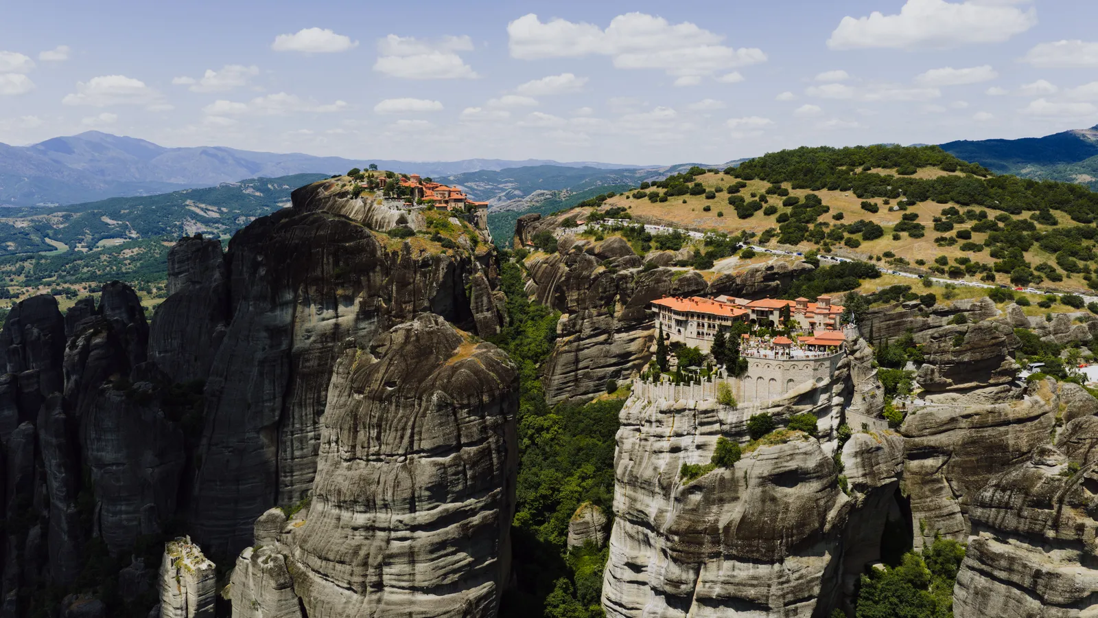 A stone monastery building on top of a sheer rock tower above a green valley