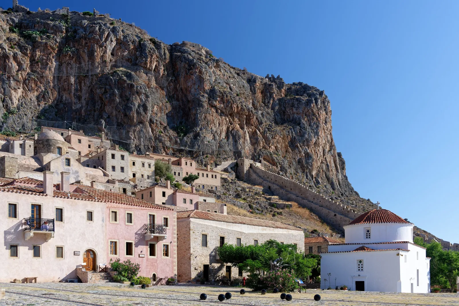 Whitewashed houses below the sheer rock face of Monemvasia with the sea beside them, Greece