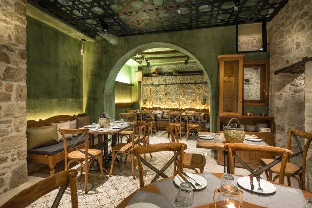 A stone hall with a central arch, green walls and wooden tables set with candles