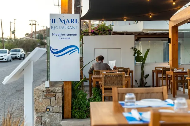 A sign on a post beside the road and behind it a terrace with wooden tables and wicker chairs