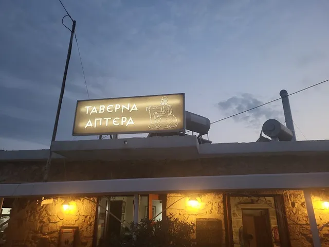 A lit Greek sign on the roof of a stone building with glowing lamps at dusk