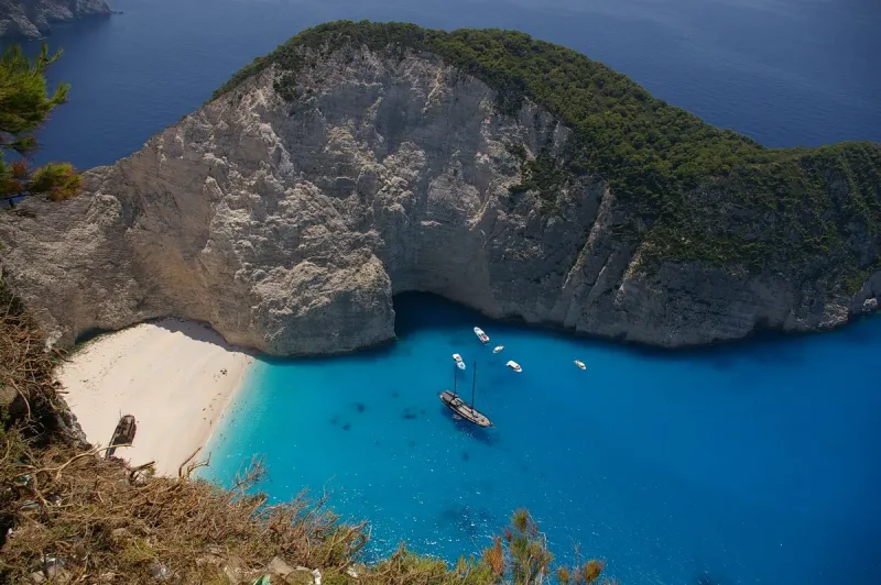 A cove ringed by white limestone cliffs, a strip of pale sand and deep blue water with anchored boats