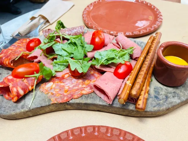 A serving board with sliced cured meats, cherry tomatoes, arugula and bread sticks