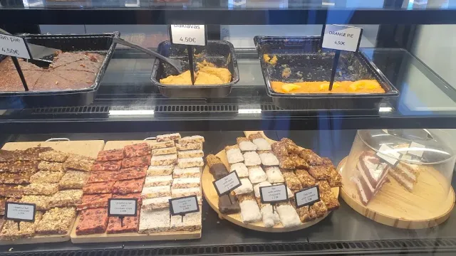 A chilled display case with trays of cakes, pastries and baklava and small price tags