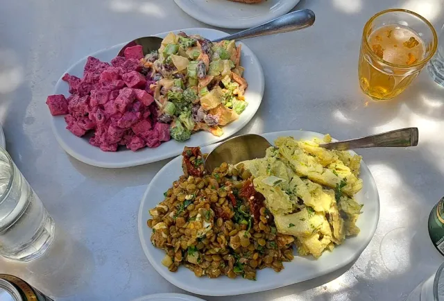 Three plates of salads on a stone table, with a glass of cold drink beside them
