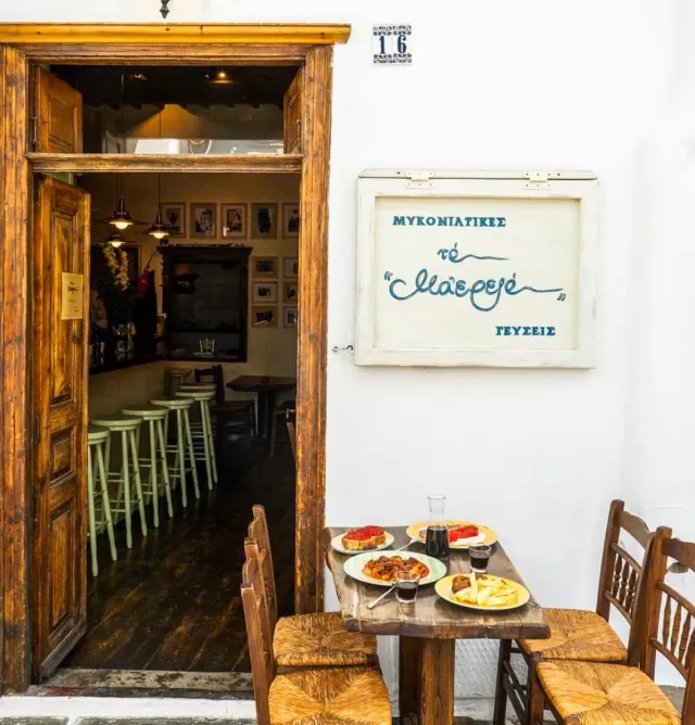 A wooden table with dishes and a wine carafe in a white alley, next to a wooden door