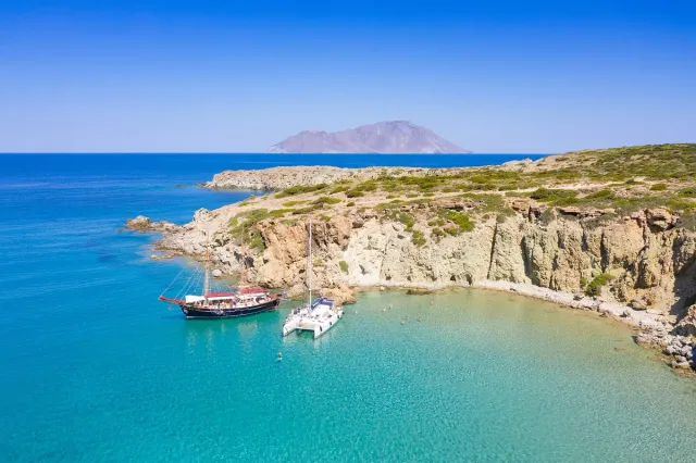Tour boats anchored in a turquoise bay below pale cliffs, with an island on the horizon