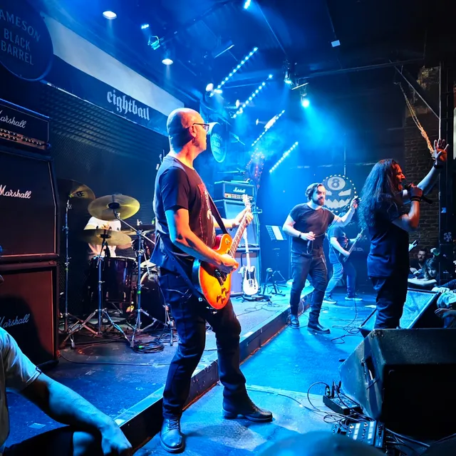 A rock band plays on a stage in blue light, with guitars and tall amplifiers
