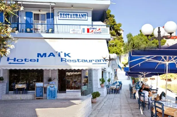 A white and blue building with signs, blue awnings and tables on the pavement beside street lamps
