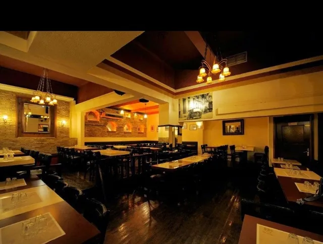 A hall set with long wooden tables, with an exposed brick wall and lit chandeliers