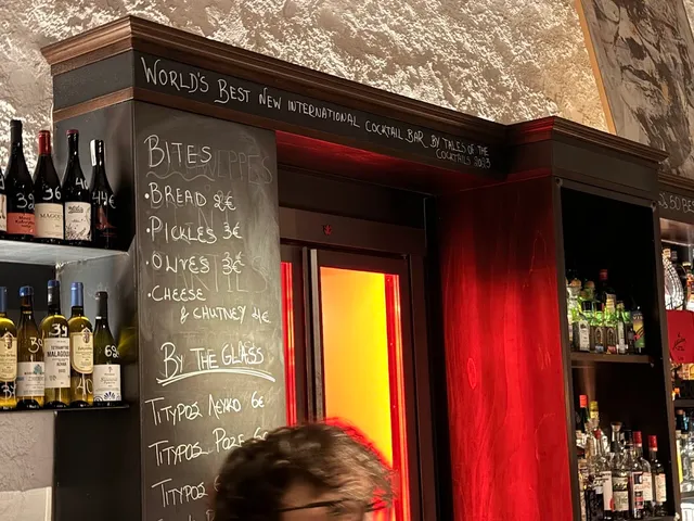 A bar counter with a chalkboard of bites and wine by the glass, and bottles on the shelves