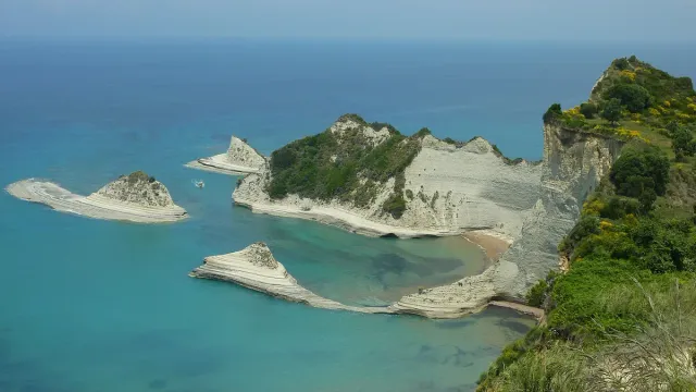 White rock spurs reaching into clear blue sea, topped with low green scrub