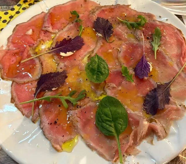 Thin slices of meat in olive oil, garnished with spinach leaves and purple arugula