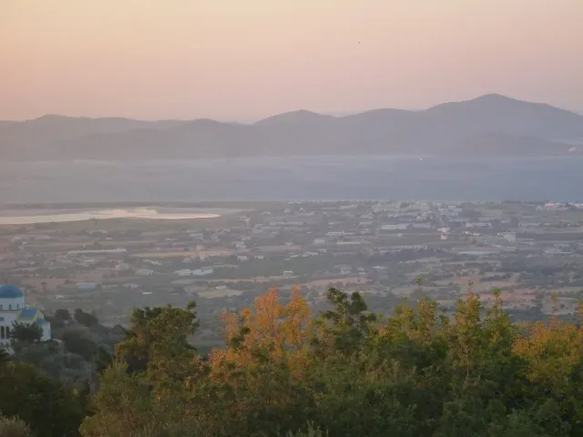 A hazy view at dusk over a plain, sea and mountains, with a blue domed church at the edge
