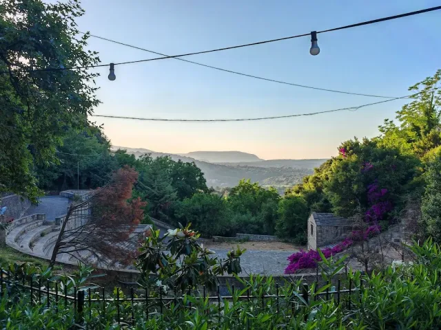 Tiered stone benches and hanging bulbs, with wooded hills and purple blossom behind
