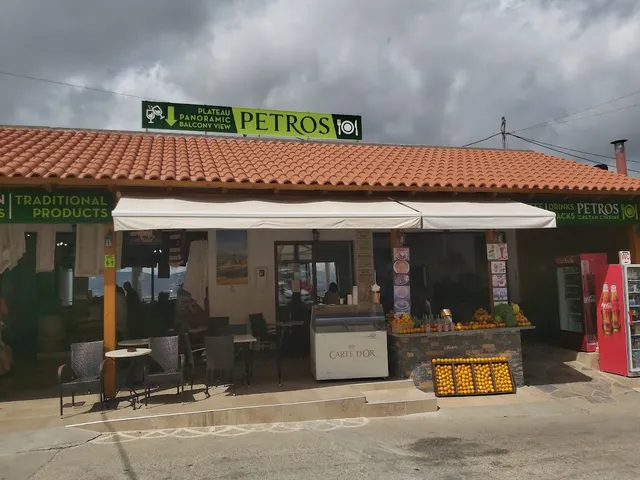 A taverna front with a tiled roof, outdoor tables and an orange stand at the entrance under cloudy skies