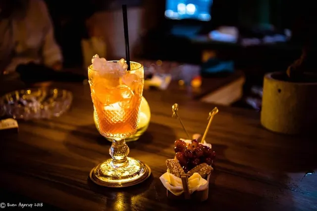An orange cocktail in a cut glass on a wooden counter in dim light