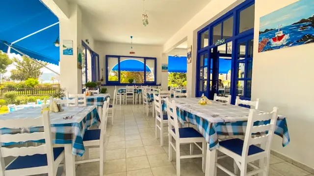 A white and blue space with checked cloths, white chairs, blue windows and sea paintings