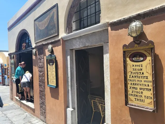 An ochre stone building with an arched opening, painted signs and visitors at the entrance
