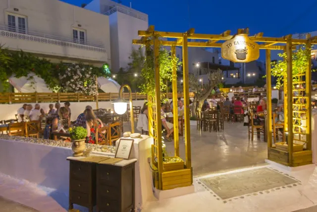 A courtyard lit in the evening with yellow wooden pergolas, a hanging sign and many diners