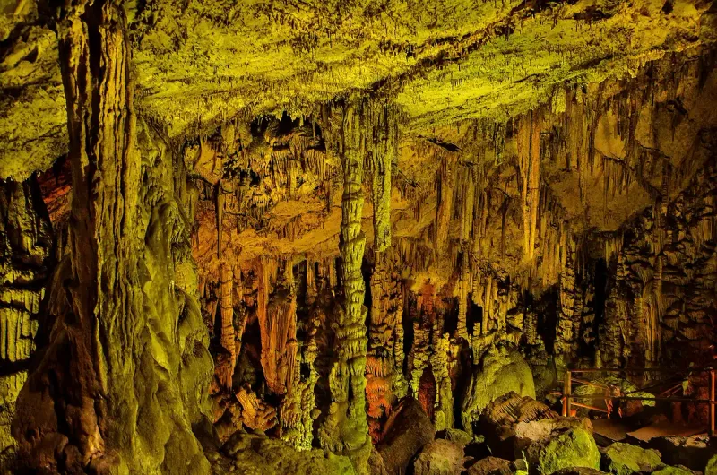 An underground cavern with long stalactites lit in golden tones