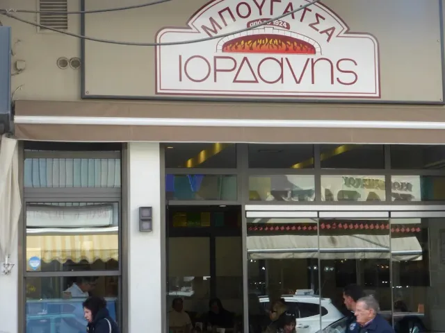 A shop front with a raised sign, a light awning and a wide display window onto the street