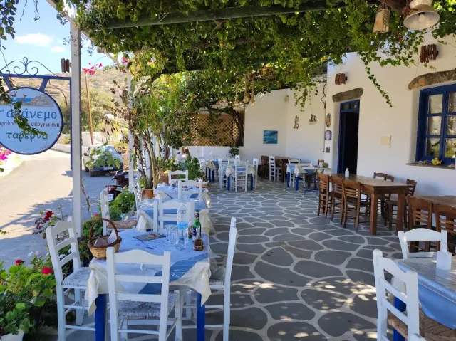 A whitewashed courtyard with a vine pergola, blue and white tables and a pebble mosaic floor