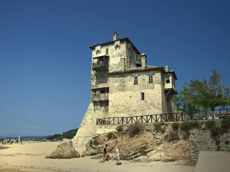 A multi storey Byzantine stone tower standing on the shore beside blue sea