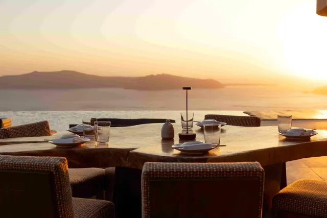 A set table facing the sea at sunset, with wide wicker chairs