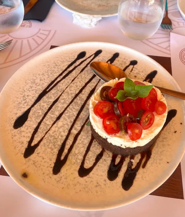 A savoury cheese cake with cherry tomatoes and basil, and lines of dark sauce on the plate