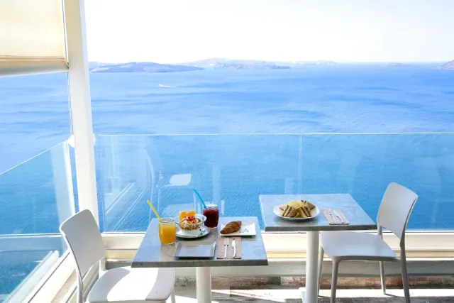 Two tables with breakfast and juice behind a glass railing, facing a blue sea