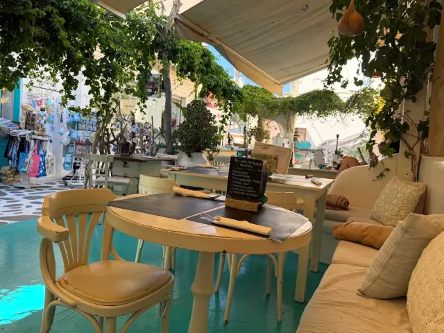 A round cream coloured table and chairs under an awning, a cushioned bench and climbing greenery