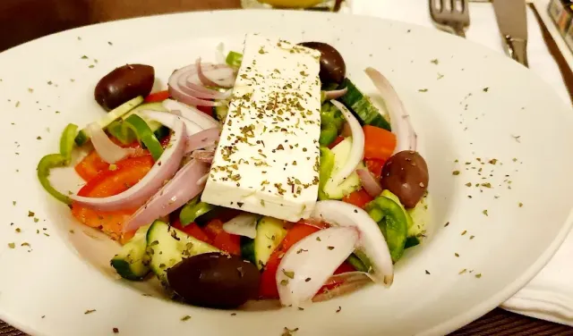 A plate of salad with a slab of white cheese, olives, tomato, cucumber and red onion