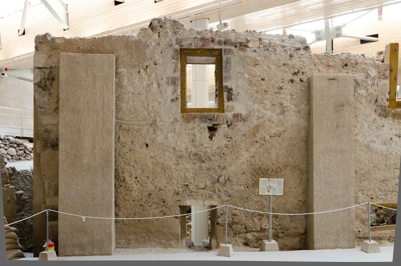 An ancient stone wall with a preserved window inside a roofed excavation