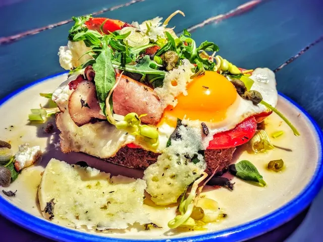 A slice of bread with a fried egg, bacon, cheese and rocket leaves on a plate