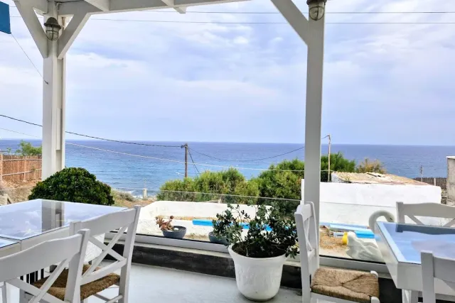A white pergola with glass tables and a large planter, facing the open sea