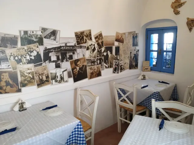 A white wall covered with old photographs, tables in checked cloths and a blue shuttered window