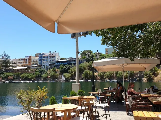 Wooden tables and parasols at the edge of a lake, with colourful houses on the slope opposite