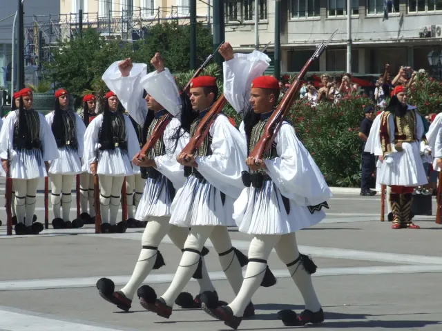Guards in traditional uniforms with red caps marching in a high ceremonial step