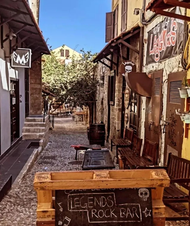 A pebble paved alley with wooden benches, painted signs and a chalkboard at the entrance