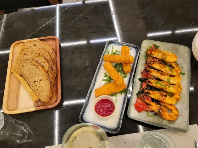 Slices of bread, fried cheese sticks and grilled prawns on a dark marble surface