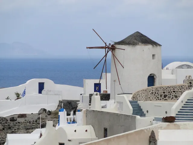 A white windmill with a conical roof above whitewashed houses and the sea