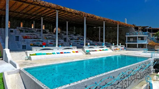 A rectangular pool with light blue water, stone steps, colourful cushions and a reed canopy