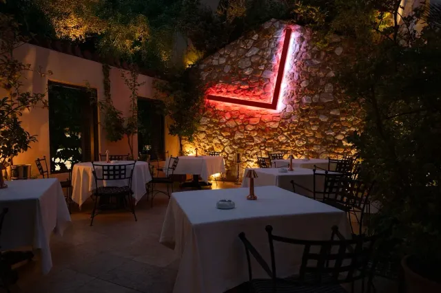 A restaurant courtyard in the evening with white tablecloths, a lit stone wall and a red light strip