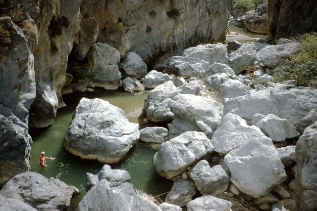 A green pool among huge white boulders in a narrow rock cleft, with a lone swimmer in the water