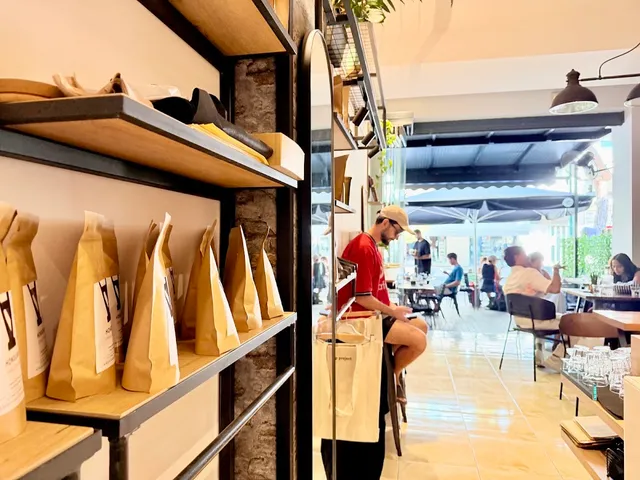 Coffee bags on wooden shelves, with a bright café and people at tables behind