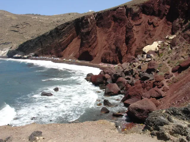 Steep red cliffs dropping to blue sea with breaking white waves